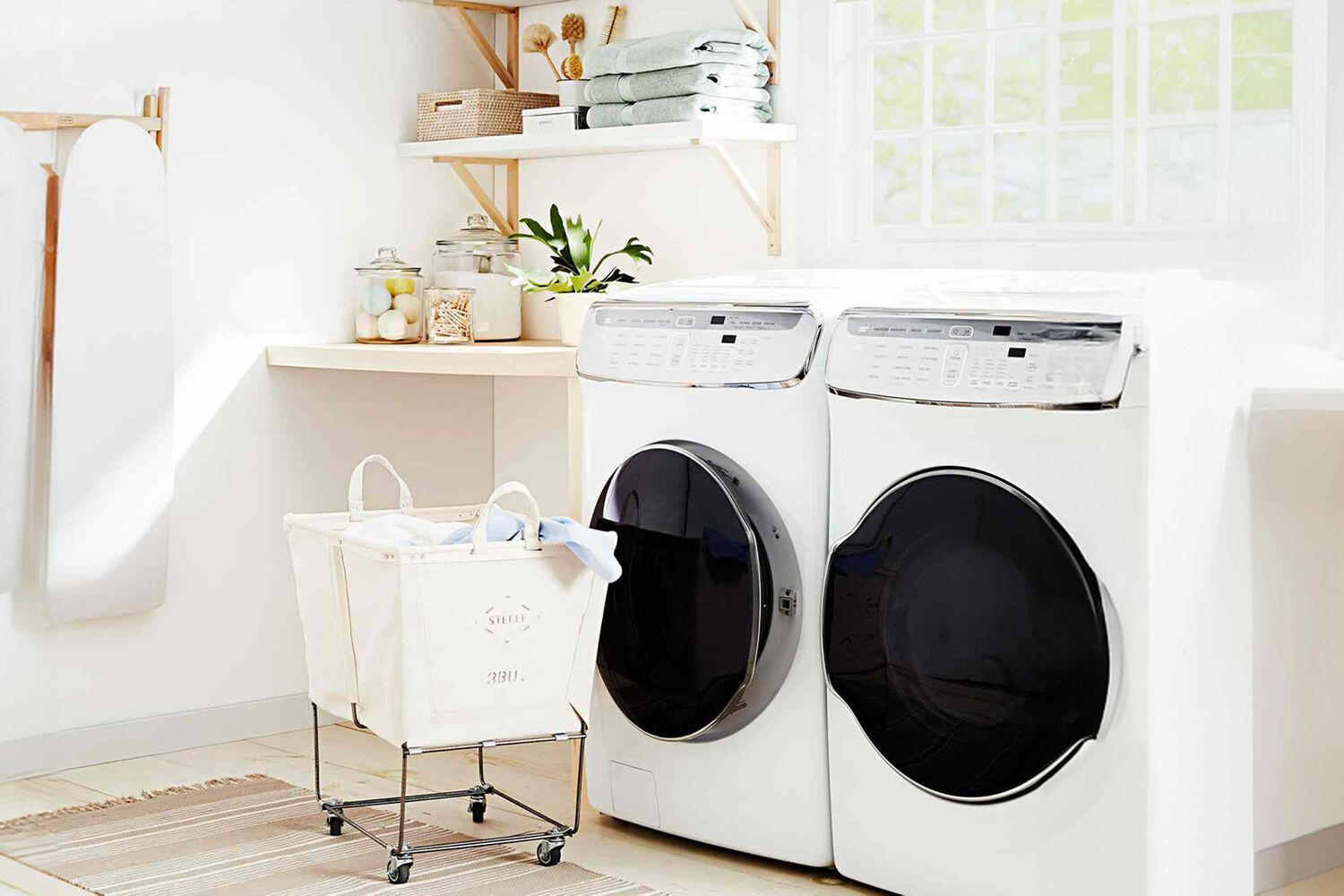 Modern laundry room with white front-loading washer and dryer machines beside a laundry basket and storage shelves.